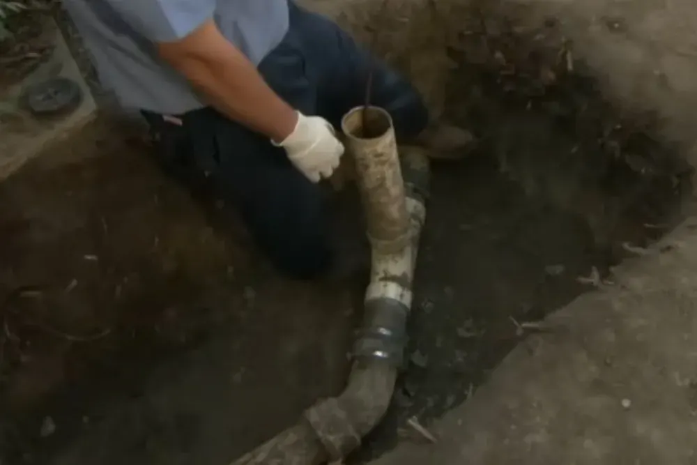 Worker in a trench reaching a cracked sewer pipe joint