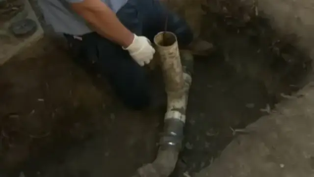Worker in a trench reaching a cracked sewer pipe joint