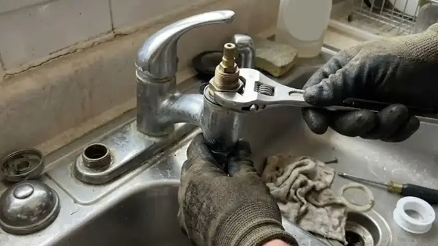 Gloved hand using a wrench on a kitchen faucet